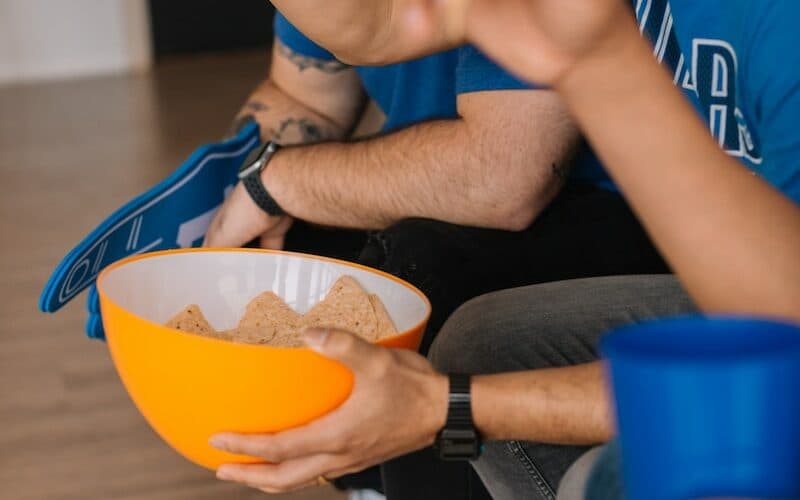 person in blue NBA Dallas Mavericks crew neck shirt sitting while holding bowl with potato chips
